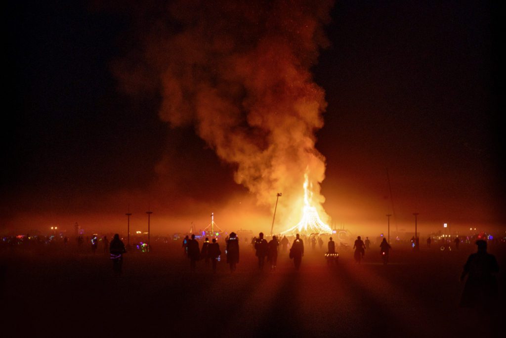 People in a small dust storm walking towards the Temple Burn at Burning Man