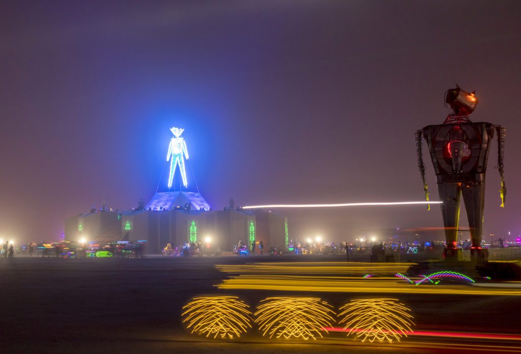 The Man at Burning Man with a robot and light trails in the foreground